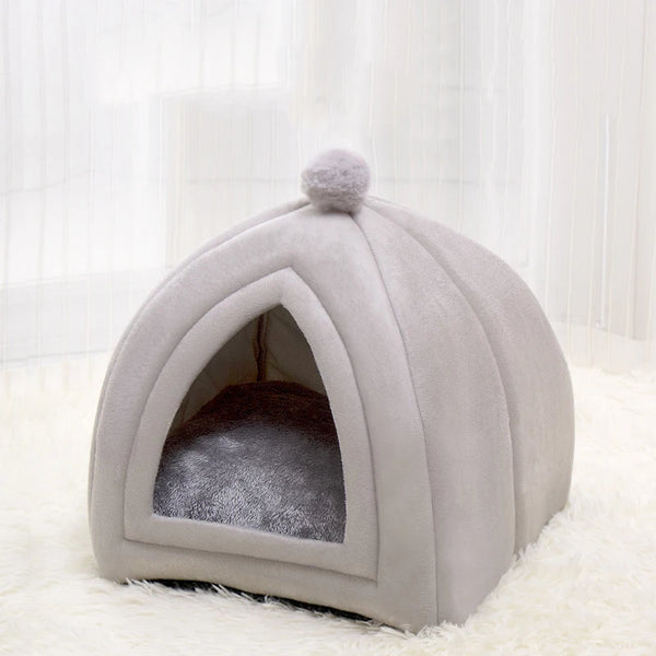 A light gray, arched cat bed cave with a fluffy top and soft interior lining on a white rug.