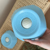 A hand holds a light blue interactive slow feeder dog bowl with textured surfaces.