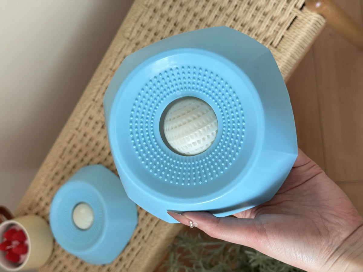 A hand holds a light blue interactive slow feeder dog bowl with textured surfaces.