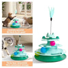 A multi-layered green and teal cat toy tower with a turntable and feather balls, shown in use with a tabby cat.