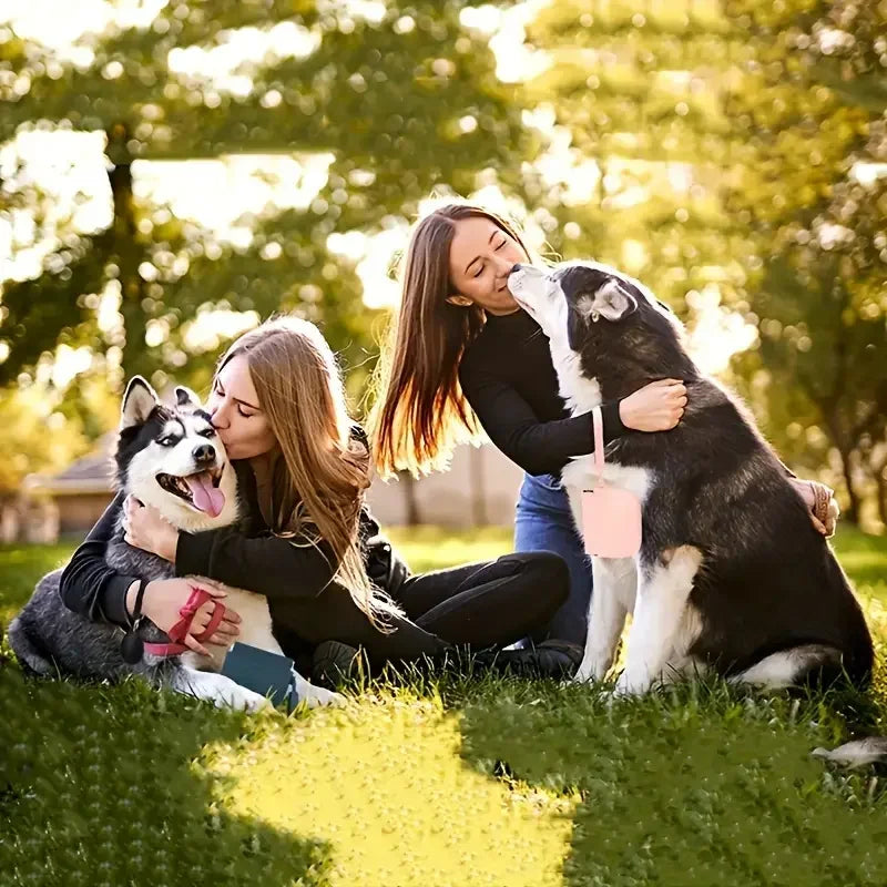 A woman is gently kissing a dog while outdoors in a sunny park setting.