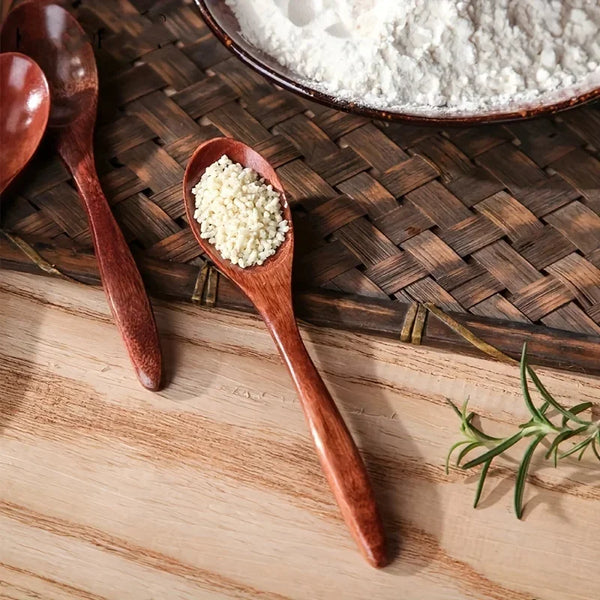 A set of six wooden tea and coffee spoons with a spoonful of white powder on one spoon, resting on a wooden surface.