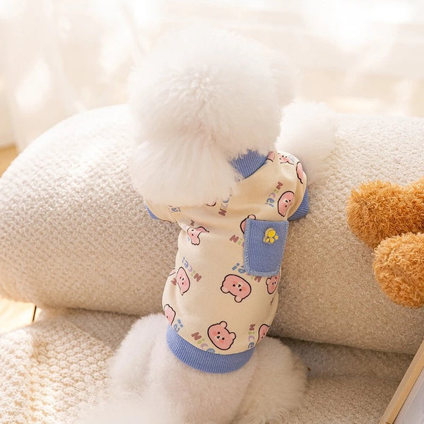 A light yellow cartoon print dog vest with a fluffy white trim is displayed on a soft, textured surface.