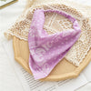 A purple bohemian paisley triangle head scarf is displayed on a light woven fabric and next to some paper.