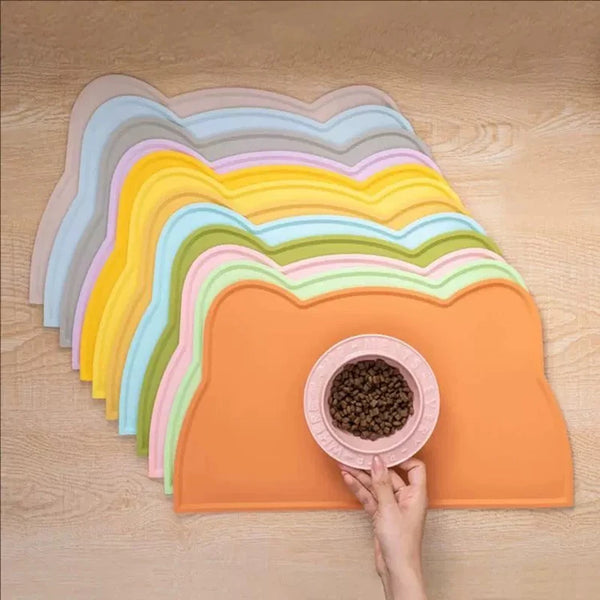 A stack of colorful silicone pet feeding mats in various shades of pastel and orange, with a hand reaching for one.