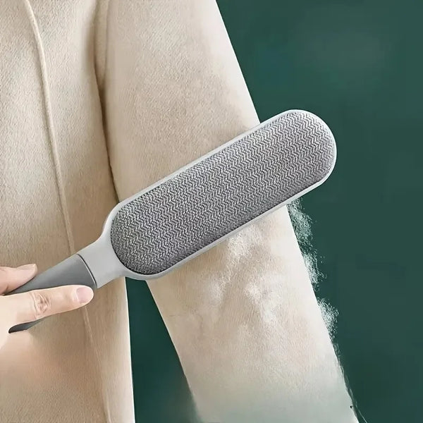 A hand holds a gray silicone pet hair and lint remover device against a light skin tone.