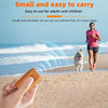 A hand holds an orange ultrasonic dog bark deterrent device on a sandy beach with a dog in the background.