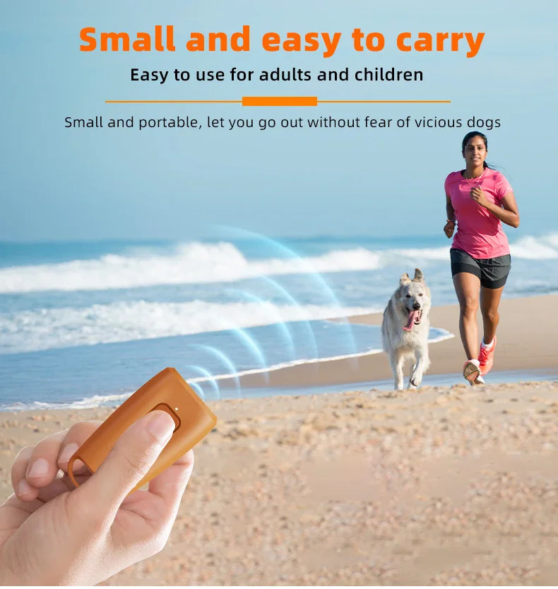 A hand holds an orange ultrasonic dog bark deterrent device on a sandy beach with a dog in the background.