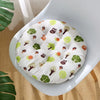 A white quilted pet bed with a colorful woodland animal pattern sits on a light-colored chair.