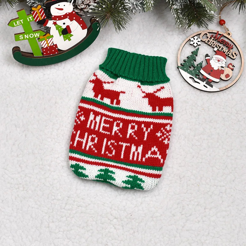 A knitted red and green dog sweater featuring reindeer and Merry Christmas patterns, displayed with holiday greenery.