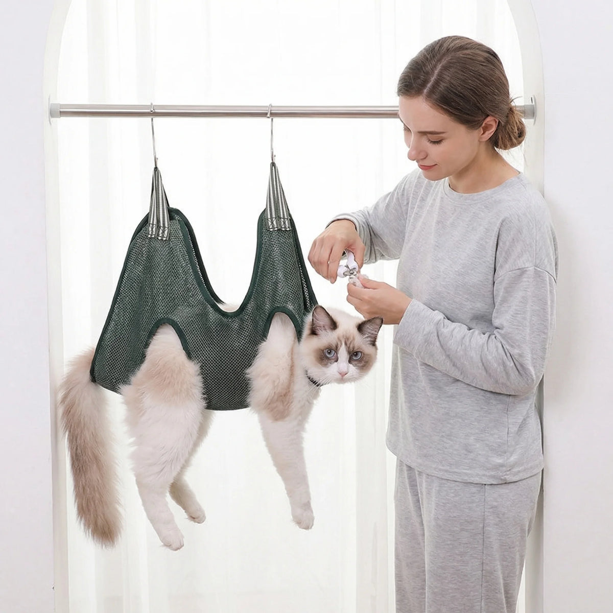 Eine Frau schneidet die Nägel einer Katze, die an einem Haustier-Grooming-Hängematte hängt.