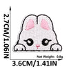 A white embroidered cat patch with pink accents shown against a measurement scale.