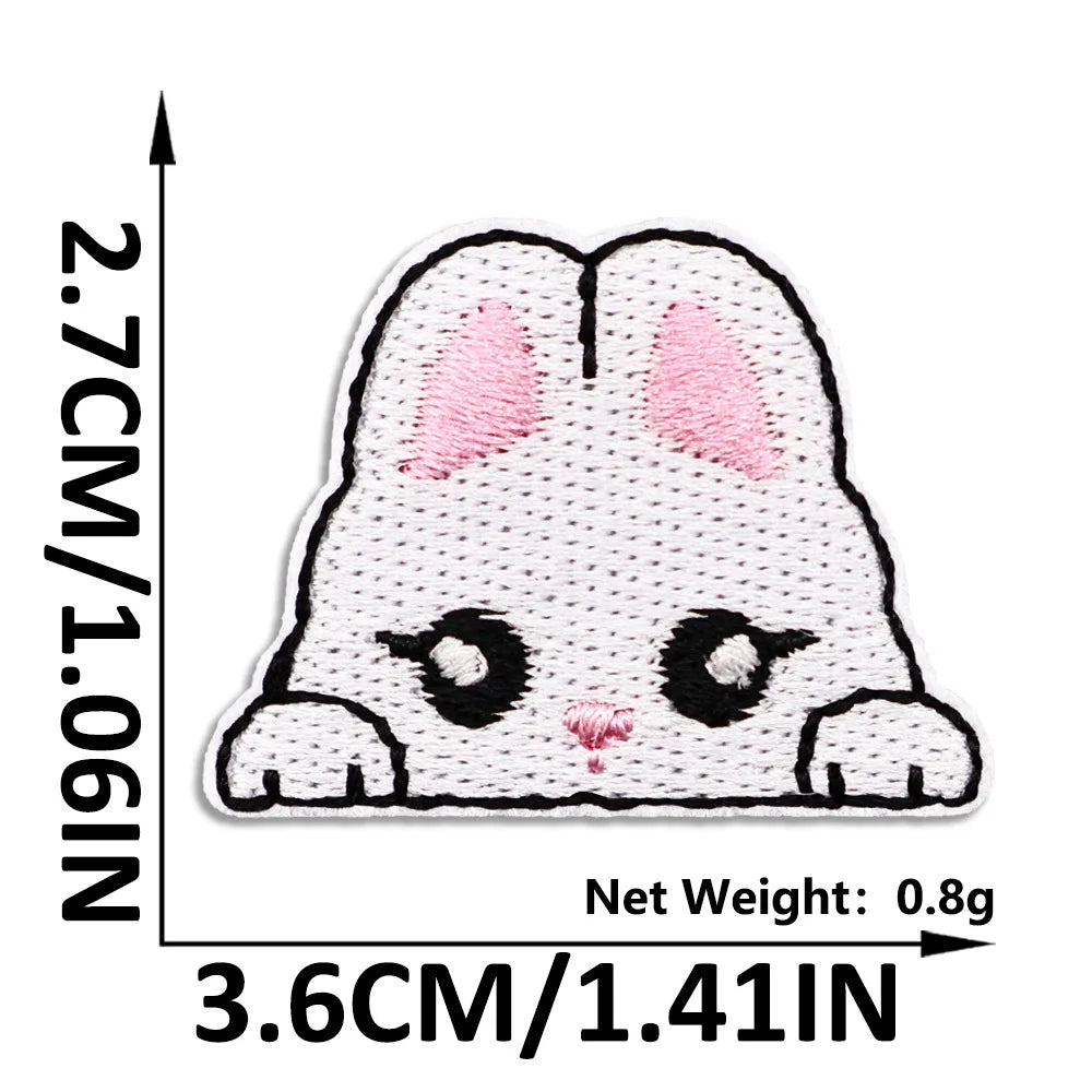 A white embroidered cat patch with pink accents shown against a measurement scale.