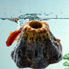 An orange fish swims near a dark, porous volcanic rock decoration in an aquarium.