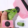A hand is holding a pink mesh bag dispenser with a green mesh bag and a black cap, next to an unincluded roll of green mesh.