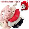 A hand holds several plush knitted dog hats in various colors including pink beige red and black