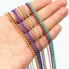 A hand holds a set of multi-colored plated ball bead necklaces, featuring various shades of pink, purple, green, and red.