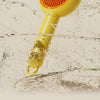 A yellow pet deshedding brush is shown submerged in water, with its orange bristles visible.