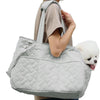 A light gray quilted portable pet carrier bag being held by a person.