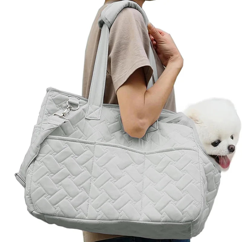 A light gray quilted portable pet carrier bag being held by a person.