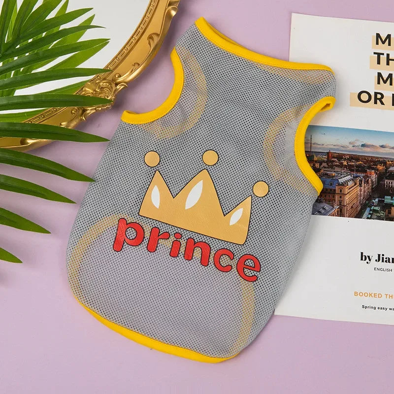 A gray mesh pet vest with a gold crown print and yellow trim resting on a pink surface.