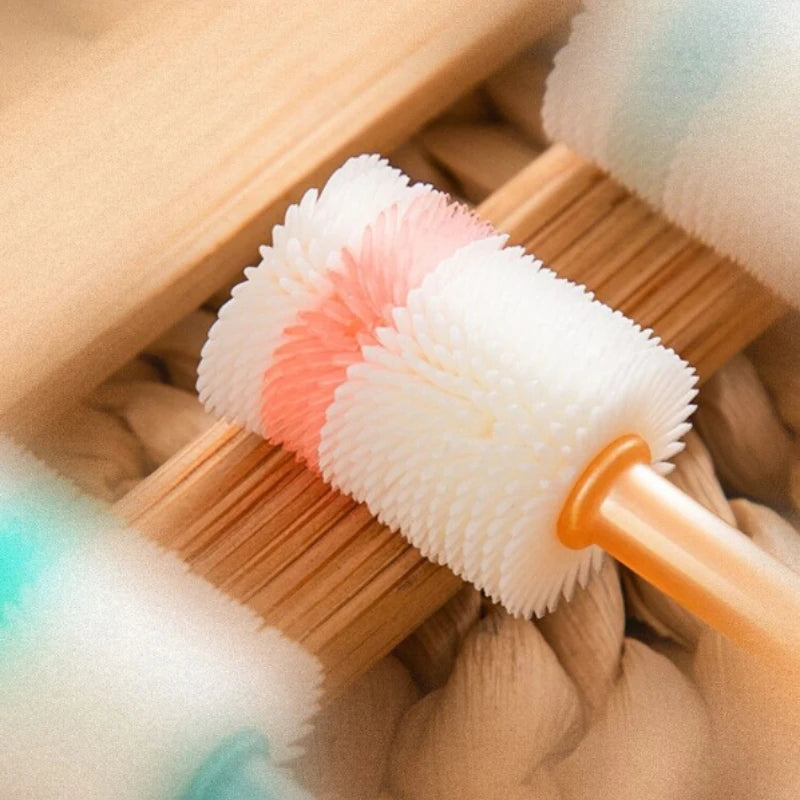 A white silicone pet toothbrush with pink accents is shown resting on a wooden brush in a textured background.