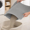A hand is pouring dry cat litter from a gray honeycomb textured mat into a white bowl.