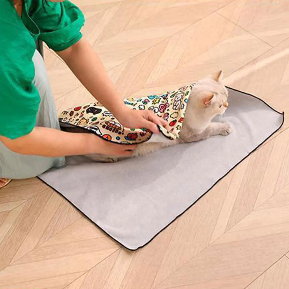 A person is gently holding a small kitten wrapped in a patterned fabric on a gray pet swaddle.