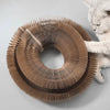 A light beige foldable accordion cat scratcher with teeth and a bell is shown next to a sleeping cat.