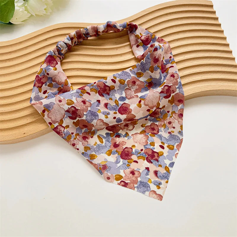 Diadema elástica o pañuelo para el cabello con estampado floral en tonos rosa, morado y crema sobre una superficie de madera 