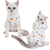A fluffy gray cat wearing a white recovery vest with various small toys on it.