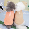 Un perro gris peludo con suéter naranja junto a un perro blanco con suéter beige.