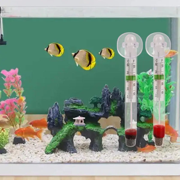 A vertical floating aquarium thermometer with a glass tube and liquid is displayed in a miniature landscape.