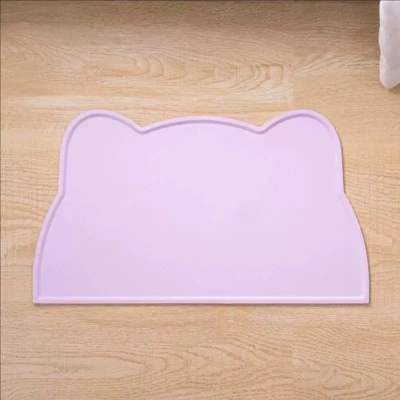 A pink silicone cat head shaped pet feeding mat resting on a light wooden surface.