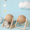 A cat is playing with a beige sisal rope ball toy resting on a wooden base against a light blue background.