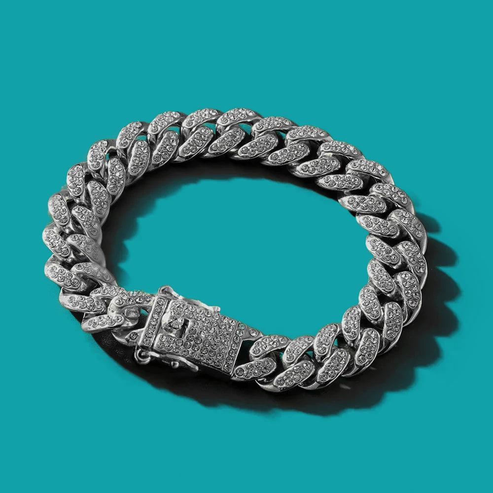 Pulsera de cadena cubana plateada con detalles de circonita, mostrada sobre fondo verde azulado.