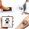A hand holds a black paw print keepsake kit with the name Savannah and a paw print tattoo on an arm.