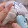 A hand holds a white pet paw being clipped by a professional nail clipper with an LED light.
