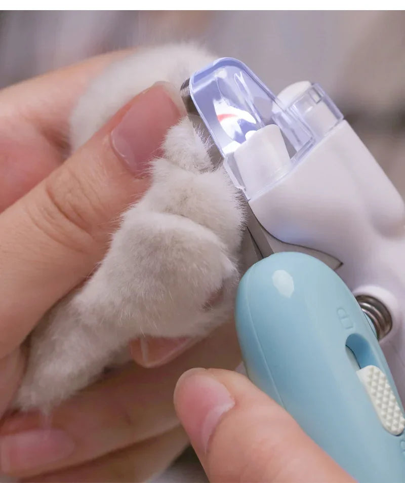 A hand holds a white pet paw being clipped by a professional nail clipper with an LED light.