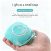 A hand holds a light blue silicone soap shape with foam, demonstrating its soft texture and small size.
