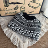 A black and white knit sweater featuring a dog pattern is displayed on a lace fabric.