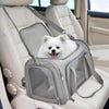 A gray travel pet carrier bag is placed on a car seat, with a white dog resting inside.