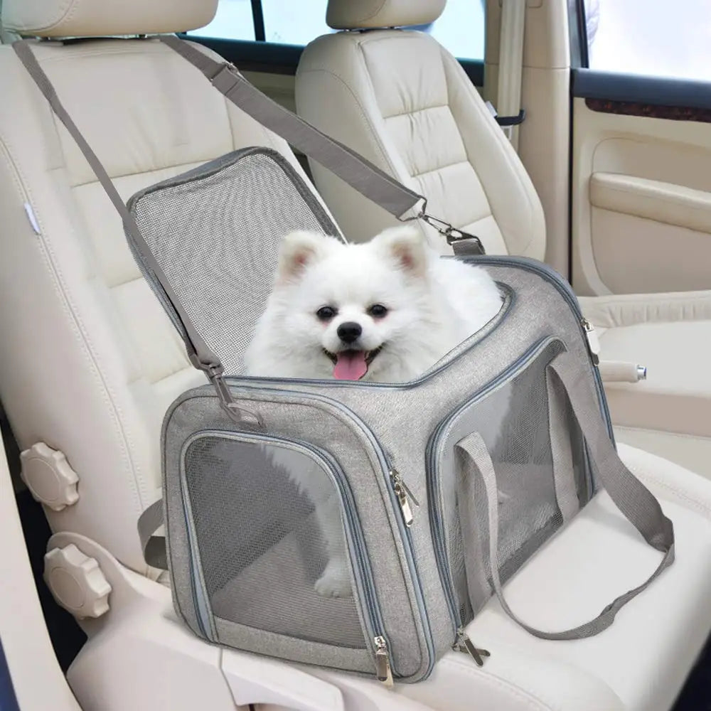 A gray travel pet carrier bag is placed on a car seat, with a white dog resting inside.