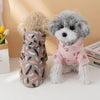 A fluffy grey dog wearing a pink waterproof summer raincoat sits next to a light brown dog.