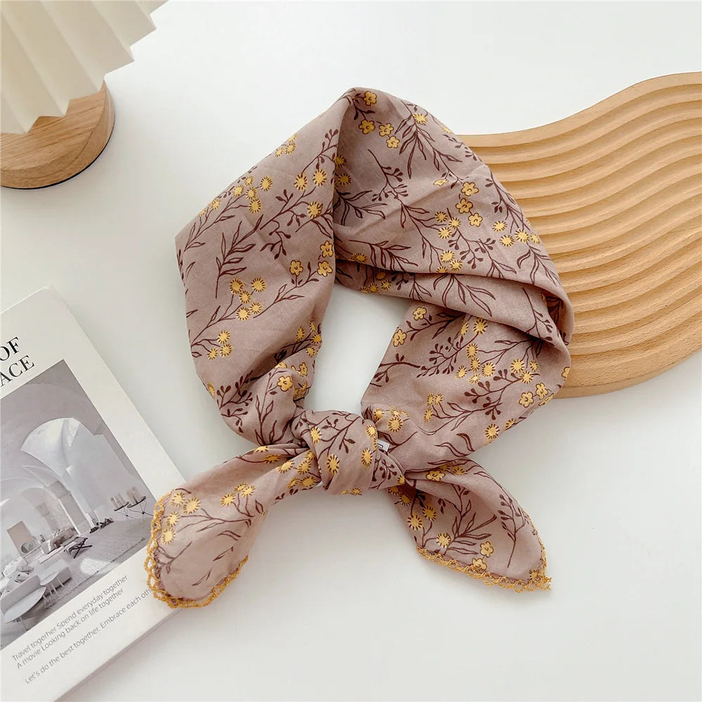 Foulard en coton beige à motif floral noué en nœud, exposé à côté d'un livre.