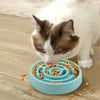 A fluffy white and brown cat is eating kibble from a blue anti-gulping slow feeder bowl.