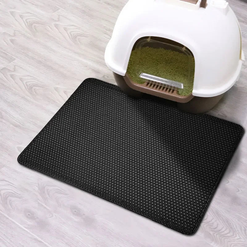 Black double-layer cat litter mat with a waterproof base placed on a light wooden floor.