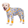A light-colored dog wearing a long-sleeved jumpsuit with a cartoon animal print featuring yellow and black figures.