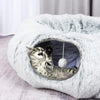 A fluffy white cat tunnel bed with a dark interior, showing a tabby kitten inside.