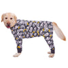 A light-colored dog wearing a long-sleeved jumpsuit with a gray and white cartoon animal print.